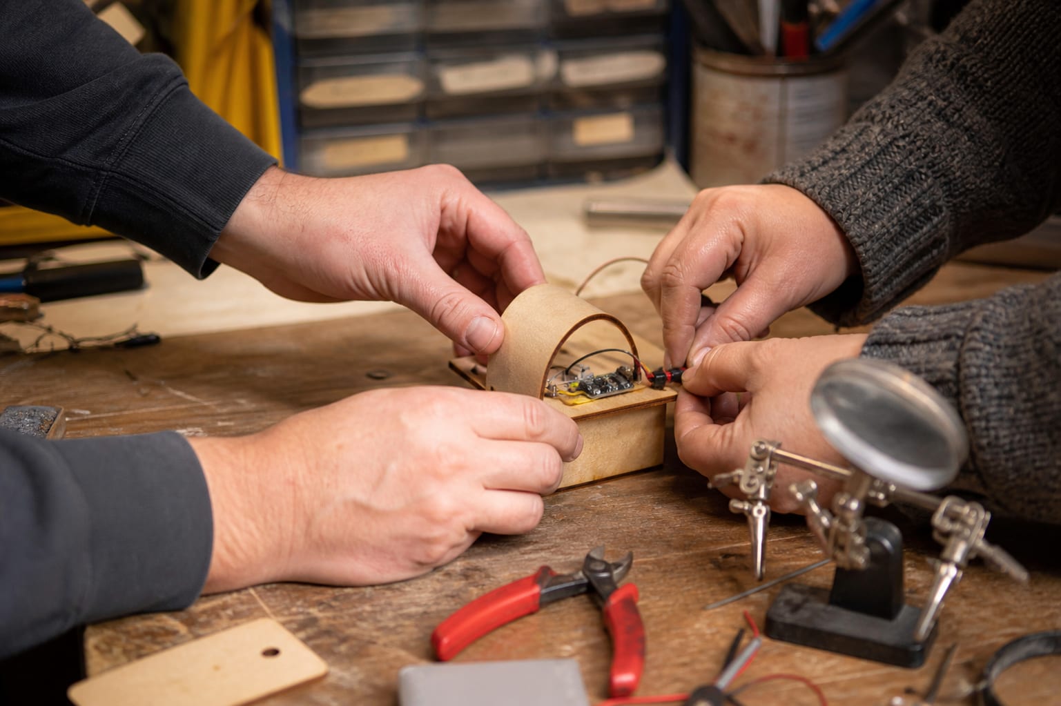 Two makers working together on a small electronics and wood prototype at a shared bench
